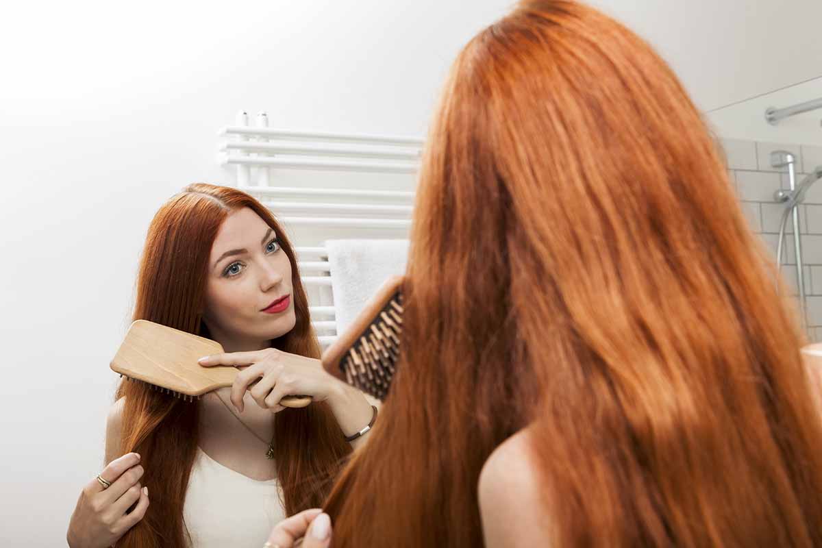 Junge Frau mit roten haaren bÃ¼rstet Ihre Haare morgens im Badezimmer