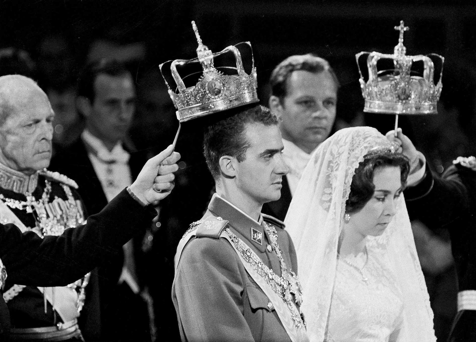 King Paul of Greece stands behind Prince Juan Carlos of Spain and Greek Princess Sophia while crowns are held above their heads during their wedding ceremony in Athens, Greece, May 14, 1962. The crowning took place during the Greek Orthodox ceremony at the Greek Orthodox Cathedral.  (AP Photo/Pool)