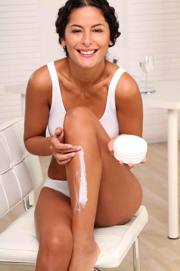 Chica poniéndose crema hidratante en la pierna