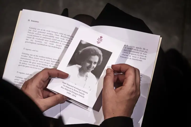 Un asistente al funeral de la Reina Fabiola sujeta entre sus manos el programa y el recordatorio con un retrato de la consorte