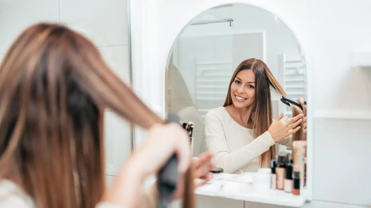 Mujer usa plancha de pelo en el baño