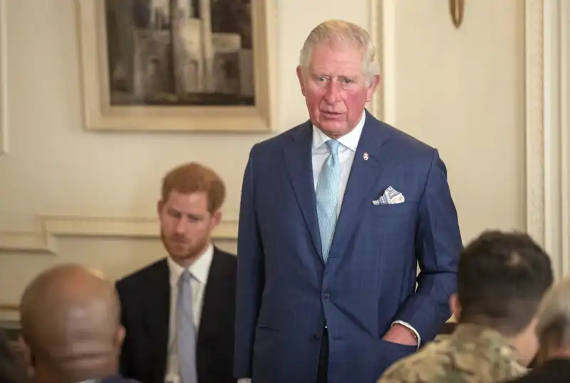 El rey Carlos III y su hijo menor, el príncipe Harry, al fondo
