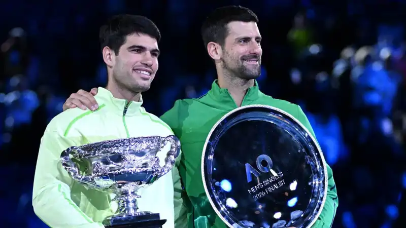 Novak Djokovic y Carlos Alcaraz mostrando sus títulos de finalista y ganador del Open de Australia, respectivamente. 